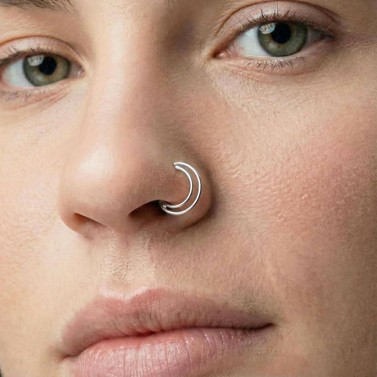 A close-up of a person's face, focusing on their nose and lips, she wears double nose silver hoops.