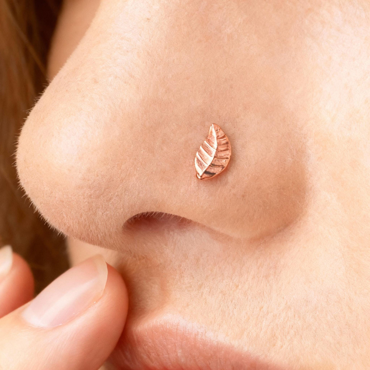 A close-up of a person's nose with a small, intricately designed leaf-shaped nose ring.