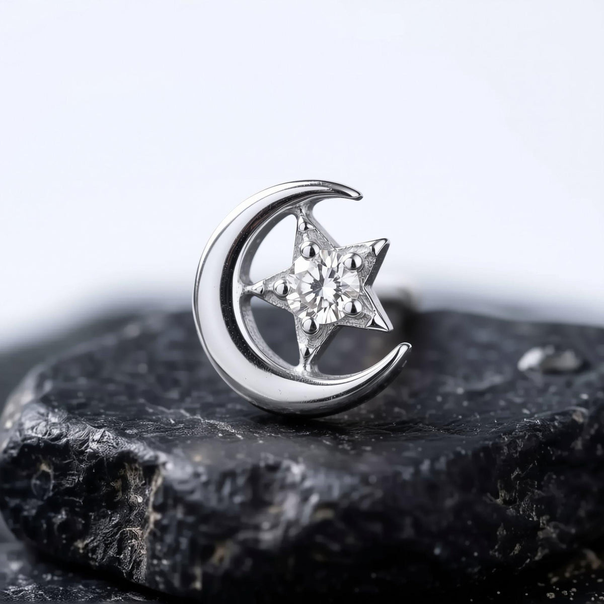 A rose gold crescent moon earring with a single diamond in the center, resting on a black rock.