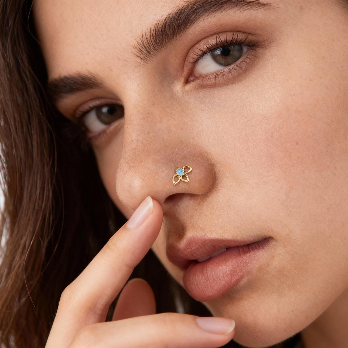 A close-up of a woman's face, focusing on her nose and fingers, with a delicate flower-shaped nose stud.