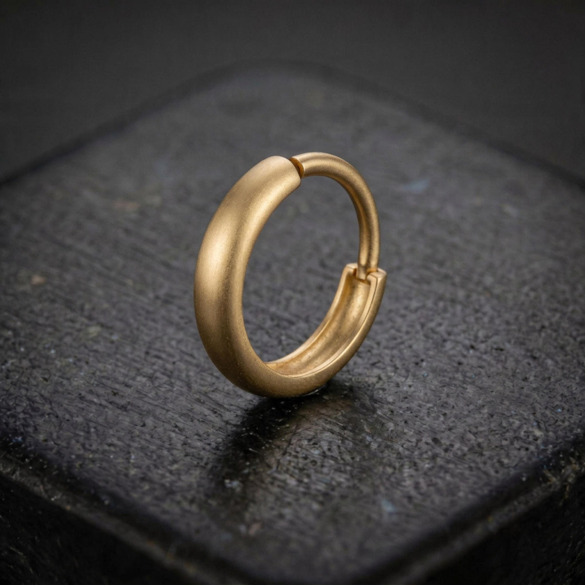 A gold-colored hoop earring is resting on a dark surface.