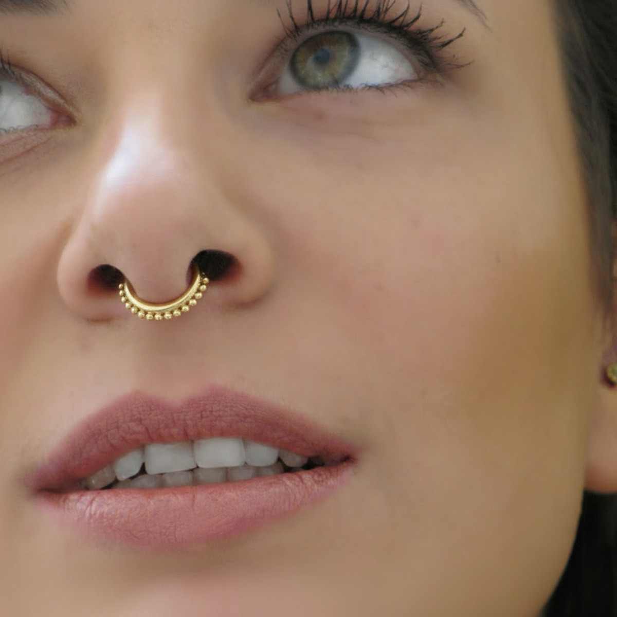 A close-up of a woman's face, focusing on her nose and lips, with a gold nose ring visible.