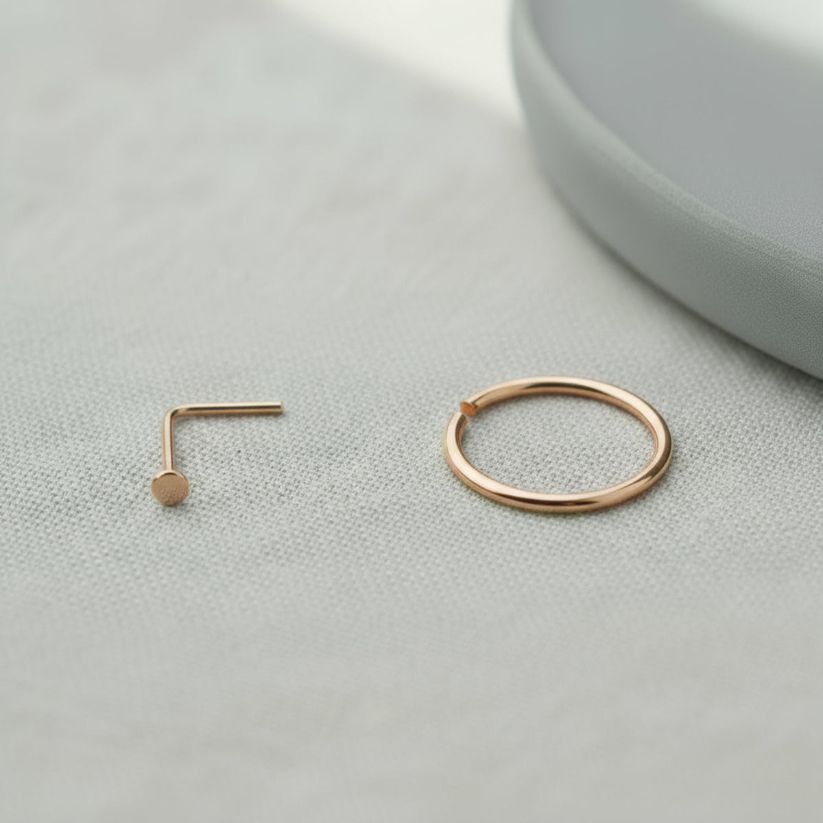 a gold-colored nose ring and a gold-colored ring on a white surface.