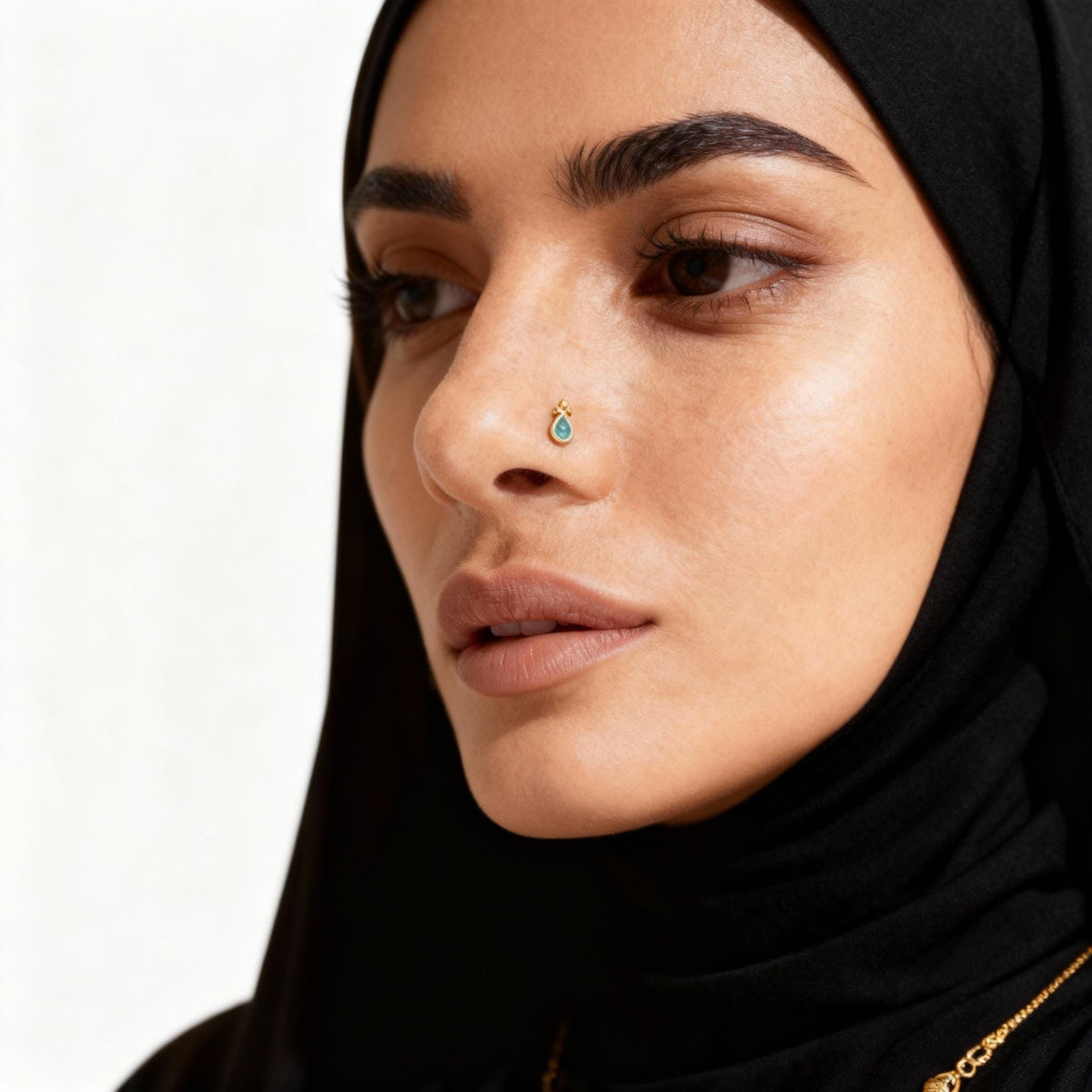 A close-up portrait of a woman wearing a black hijab and a nose ring.