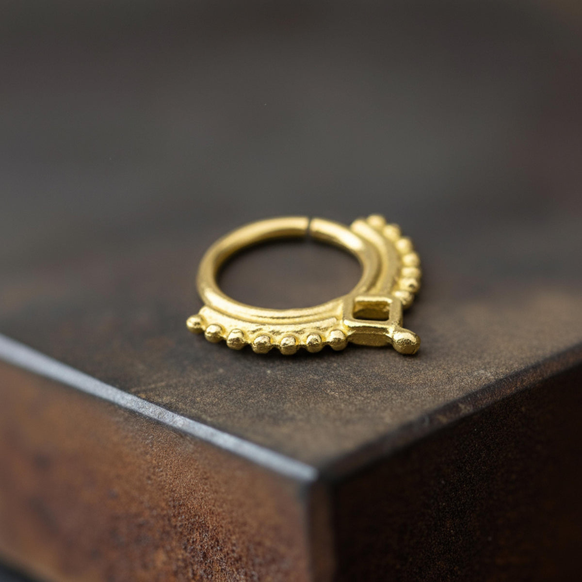 A close-up image of a gold-colored metal ring or earring resting on a dark surface.
