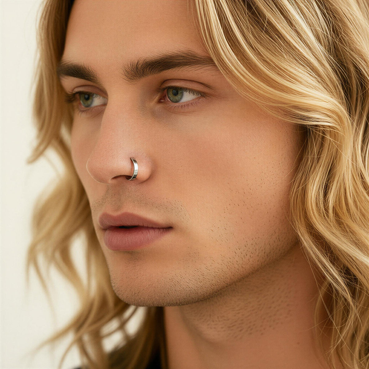 A close-up portrait of a young man with long, wavy blonde hair and a nose ring.