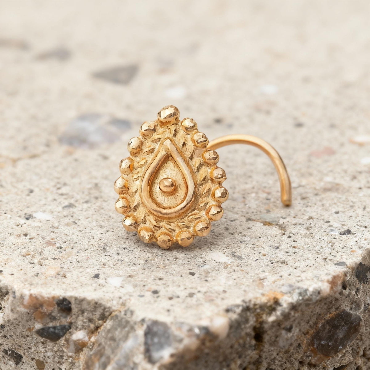 A gold-colored nose ring with an intricate design sits on a concrete surface.