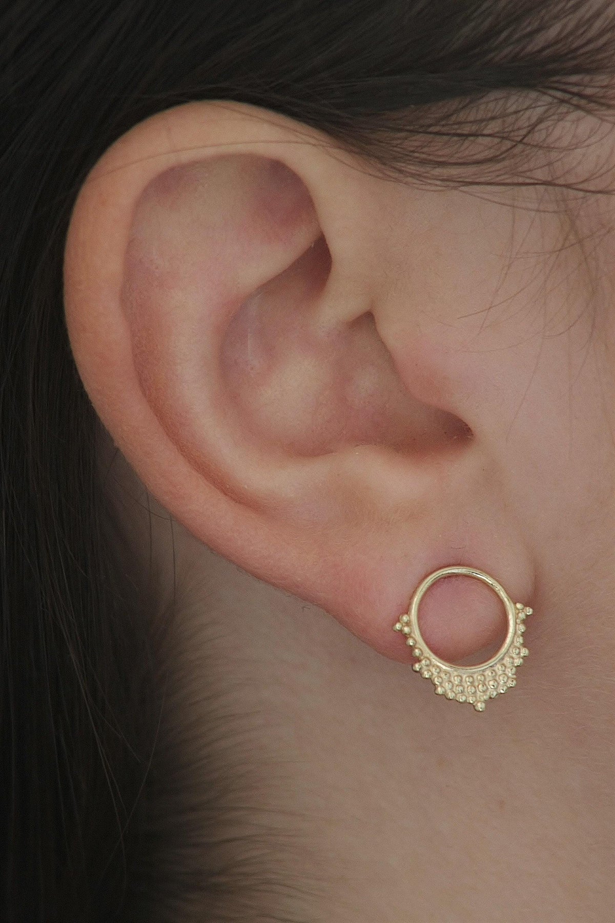 A close-up view of a person's ear, showing a gold earring with a circular design and small embellishments.
