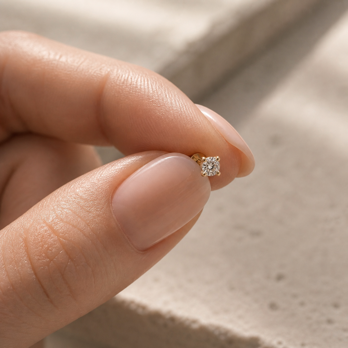 A person's hand holding a small gold-colored diamond earring.