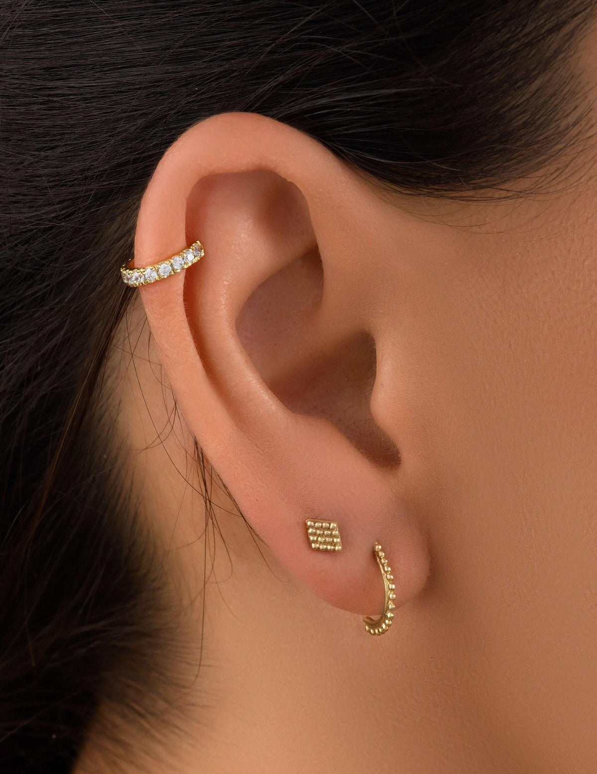 a close-up view of a person's ear adorned with two gold earrings.
