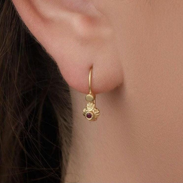 14k Gold Ruby Earrings: A close-up view of a person's ear adorned with a gold earring featuring a small floral design.
