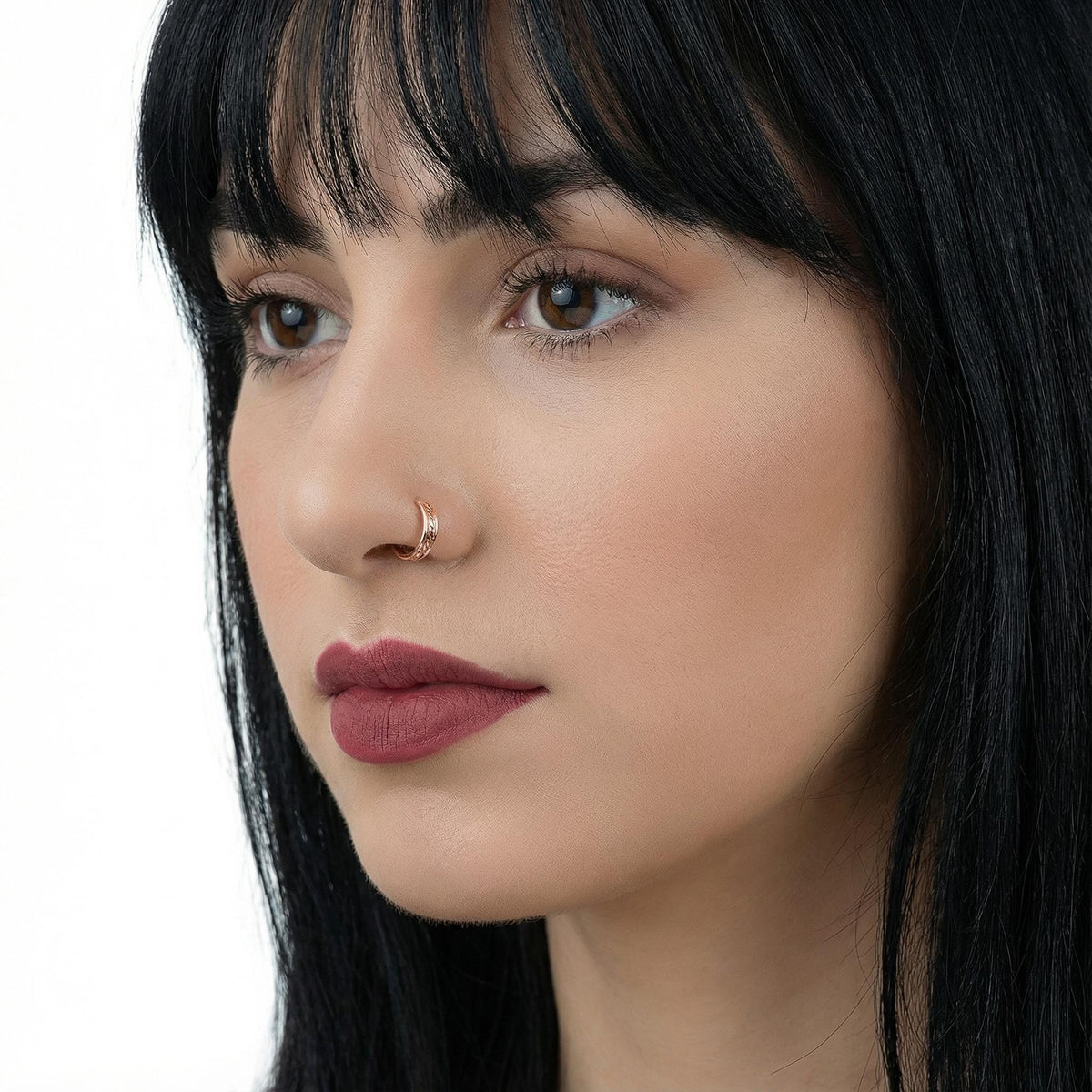 A close-up portrait of a woman with long, dark hair and a nose piercing, wearing a red lipstick look.