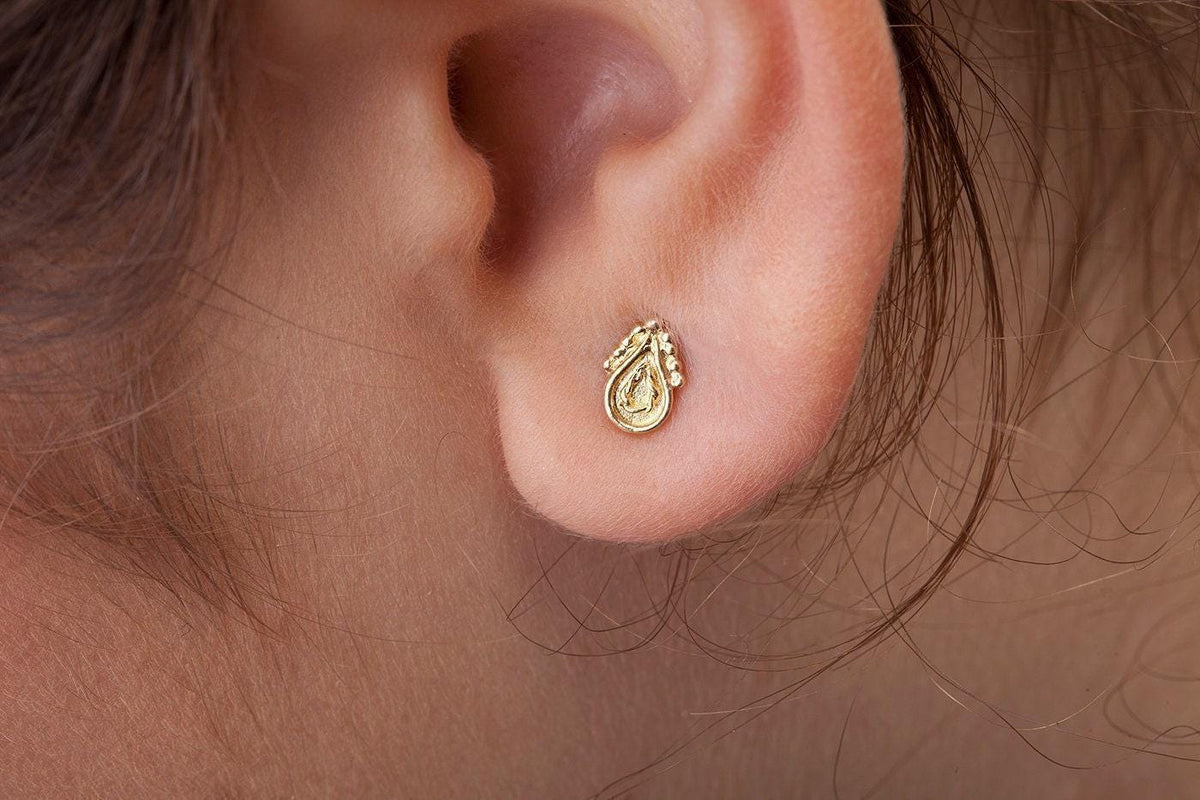 A gold earring with a small, intricate design is visible in the person's ear.