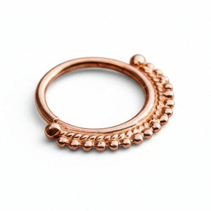 A copper-colored ring with a decorative band of small balls or beads around the edge, resting on a concrete surface.