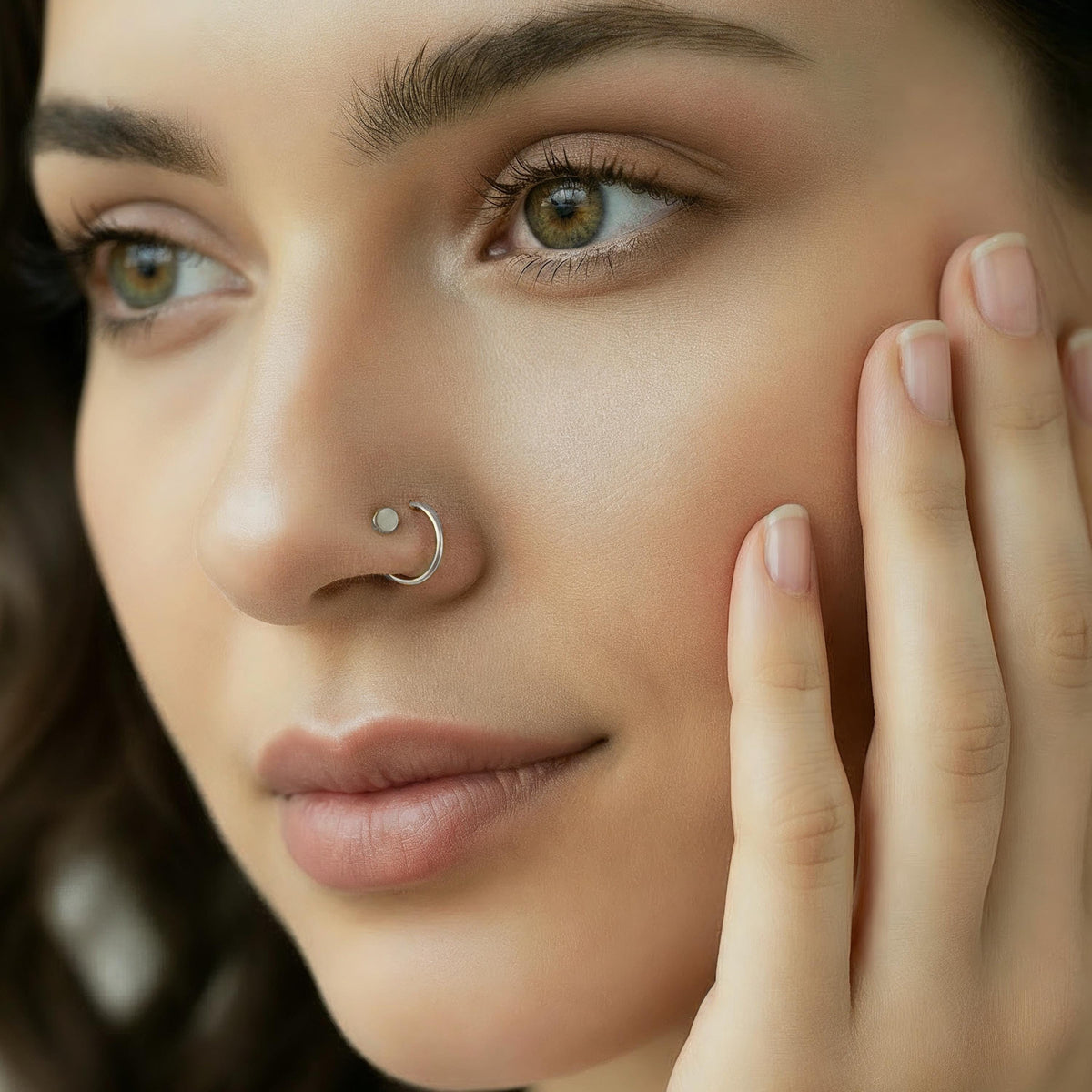 A close-up portrait of a woman with a nose ring, looking directly at the camera with a thoughtful expression.