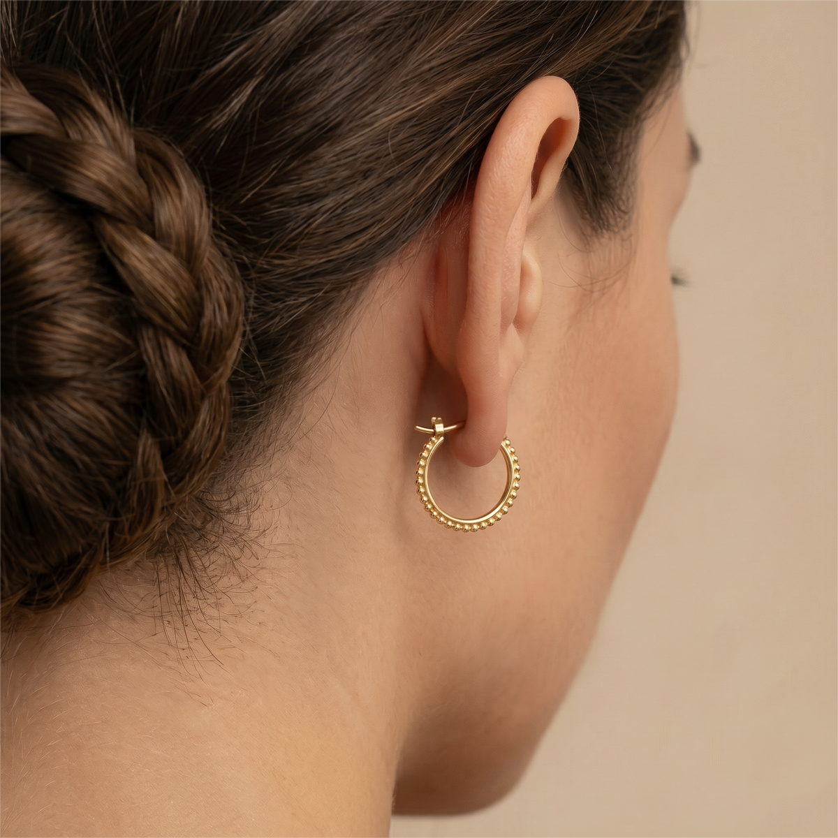 a close-up view of a woman's ear adorned with a gold hoop earring.
