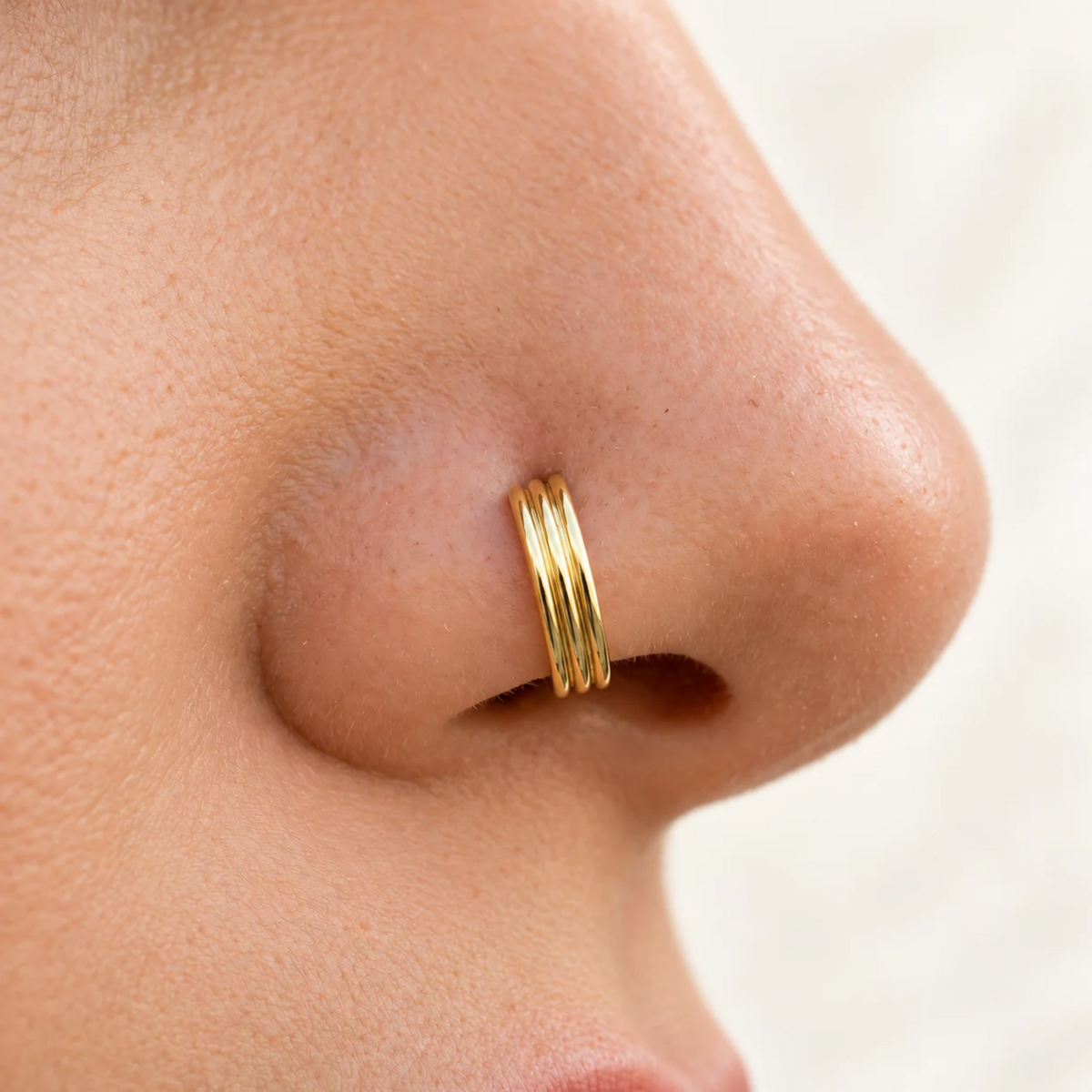 A close-up of a person's nose with a gold-colored nose ring.