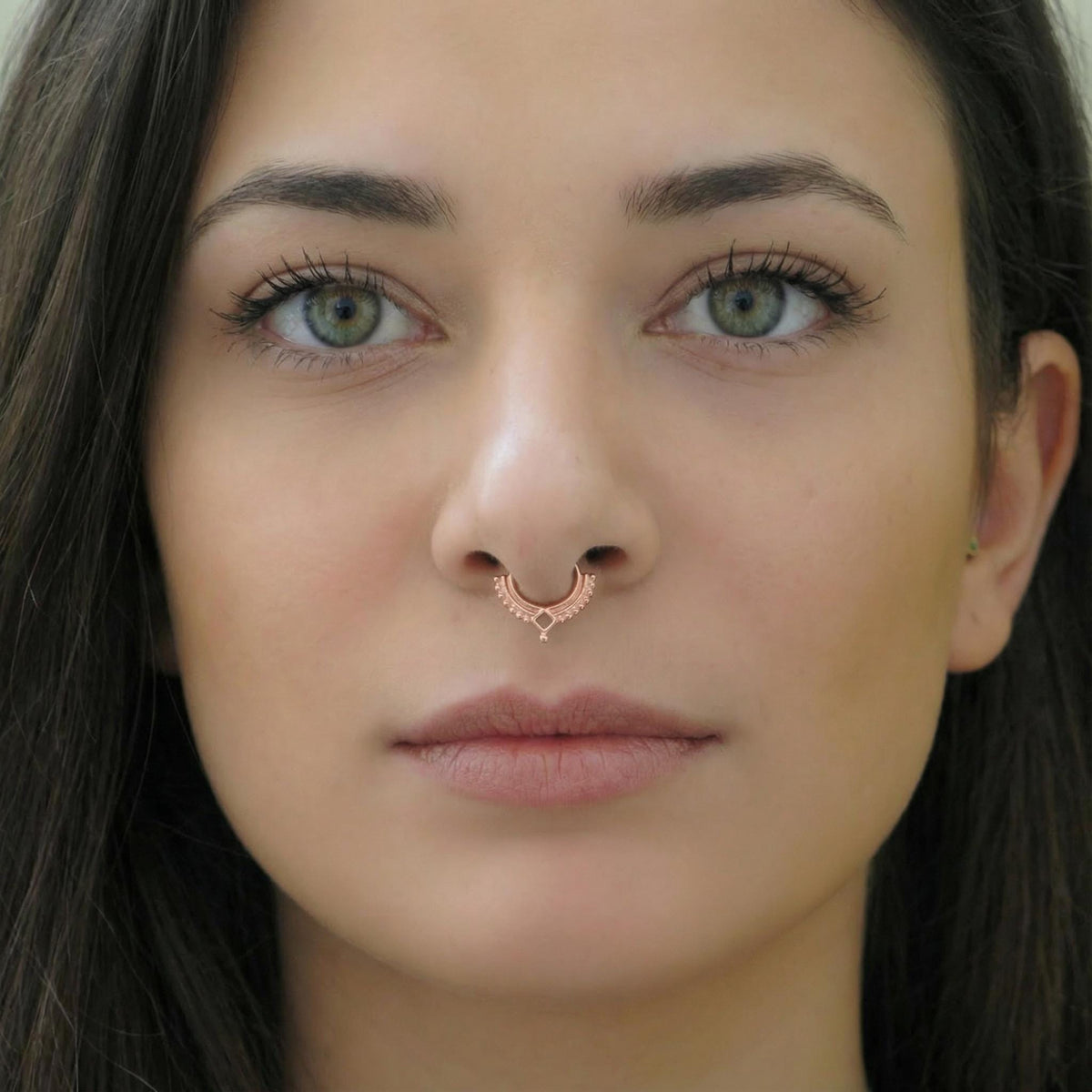 A close-up portrait of a woman with long dark hair and piercing green eyes, wearing a nose ring.
