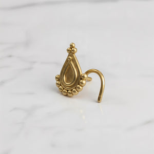 A gold-colored ornate earring or ear cuff is displayed on a white marble surface.