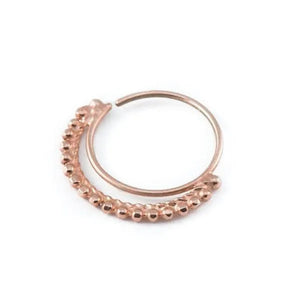 A copper-colored metal ring with a curved design and a row of small, round beads or stones along the edge.