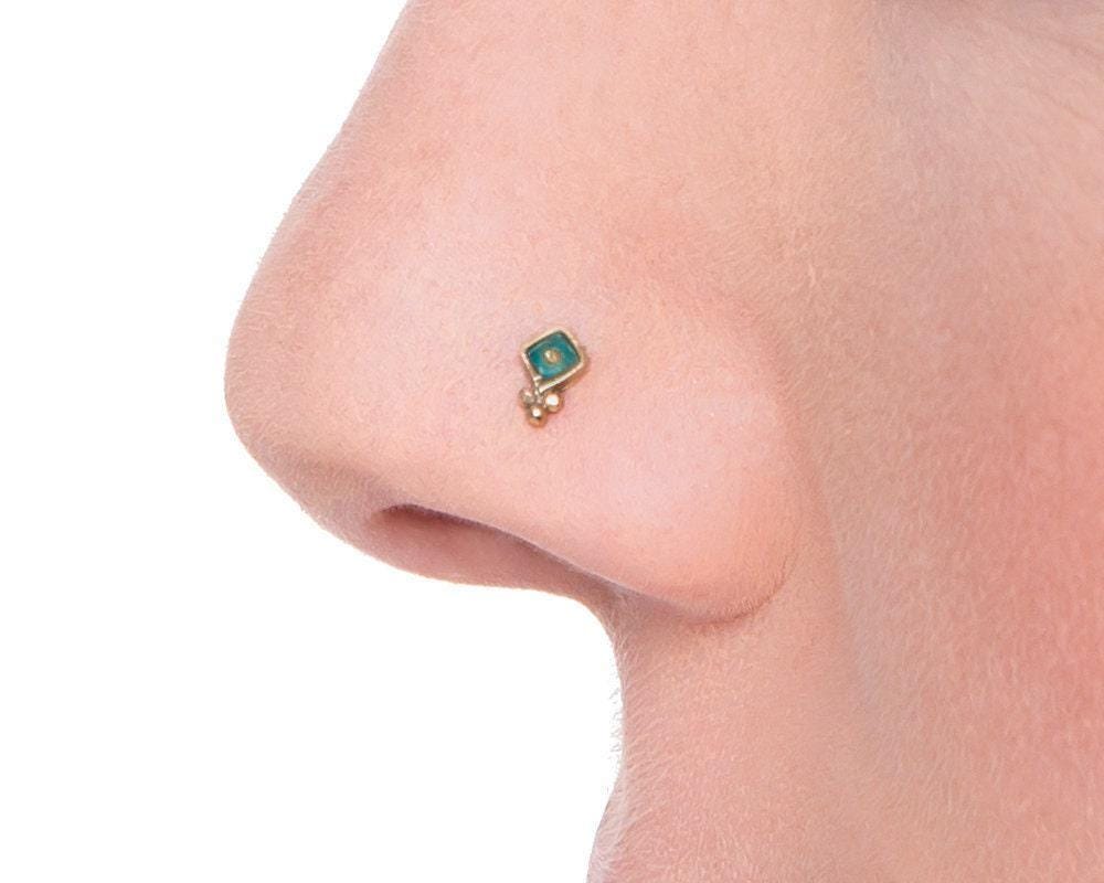 A close-up of a person's nose with a small, green-colored nose stud or piercing.