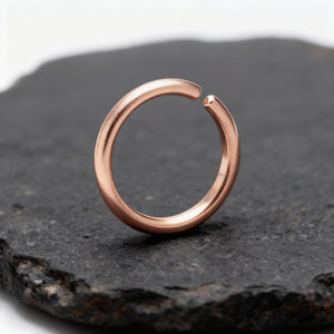 Rose Gold Nose Hoop: A copper-colored ring with a twisted shape is resting on a dark surface.