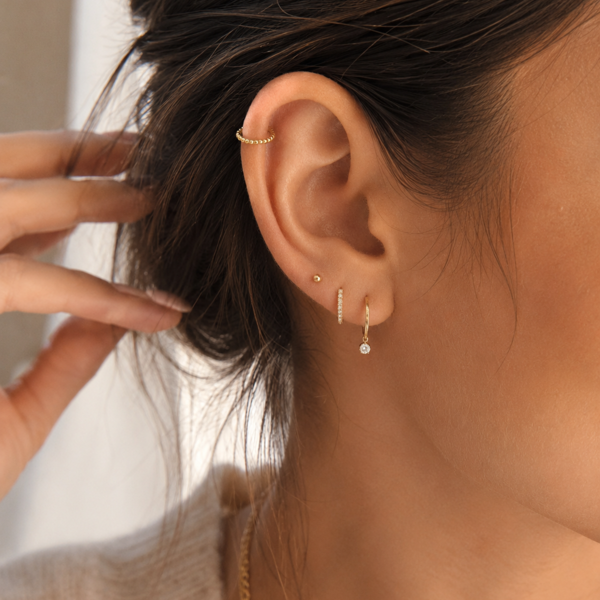 A close-up view of a person's ear adorned with multiple gold earrings, including a hoop earring and dangling earrings.