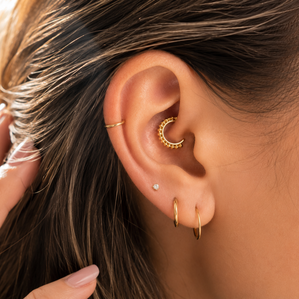 A close-up view of a person's ear adorned with multiple gold earrings, including a hoop earring and a small diamond earring.