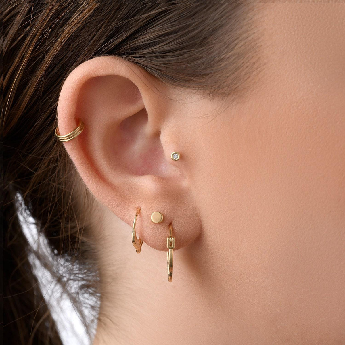 A close-up view of a person's ear adorned with multiple gold earrings, including a hoop earring, a stud earring, and a small diamond earring.