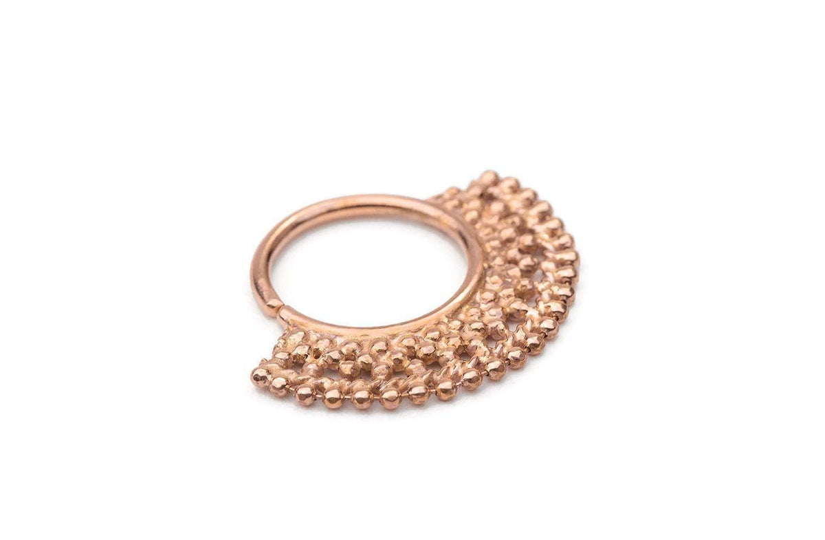 A close-up image of a gold-colored metal piercing ring with a decorative, textured design.
