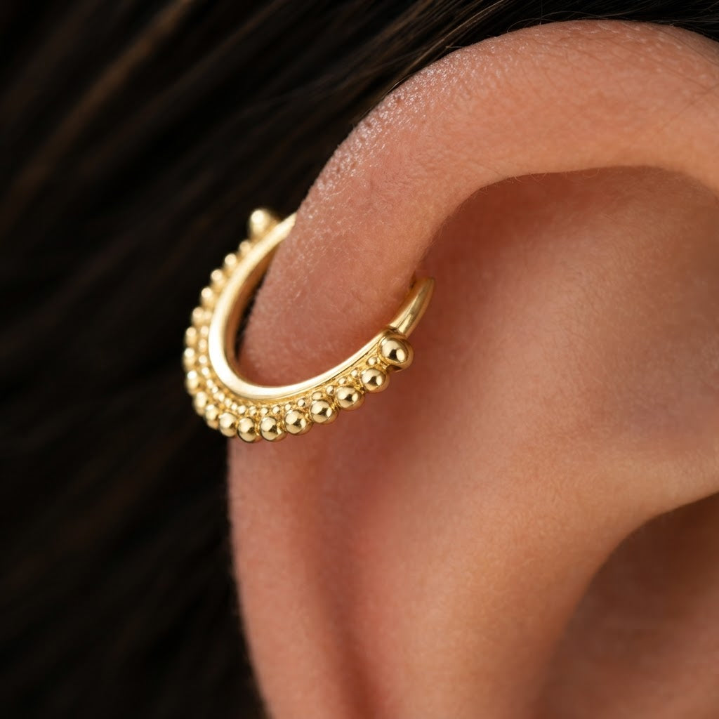 A close-up view of a gold-colored earring with a decorative design, featuring small balls or beads around the edge.