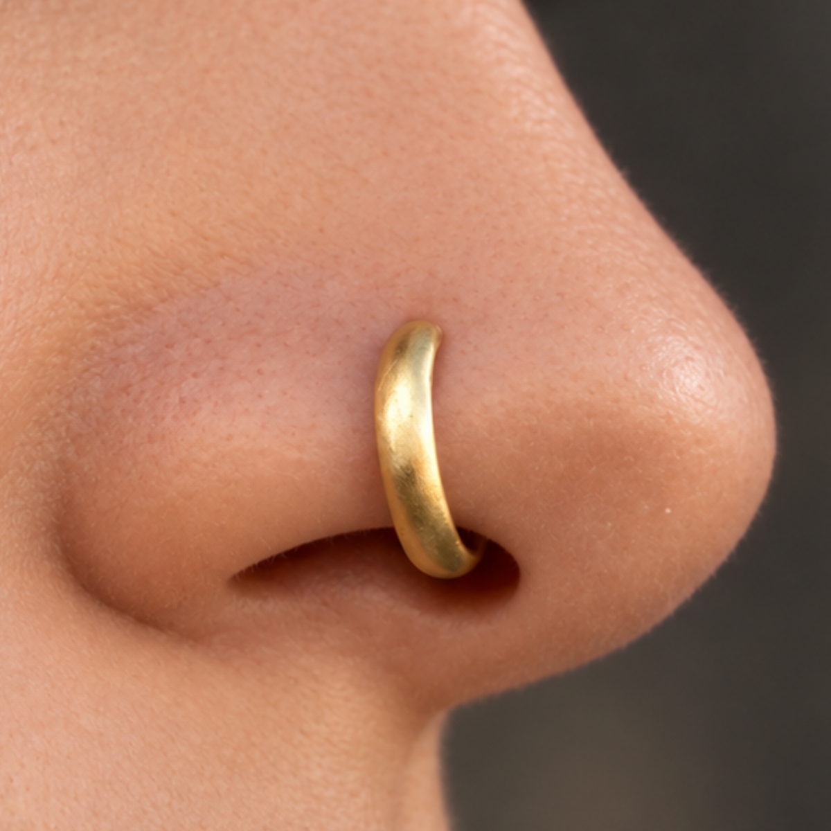 A close-up of a person's nose with a gold-colored nose ring.