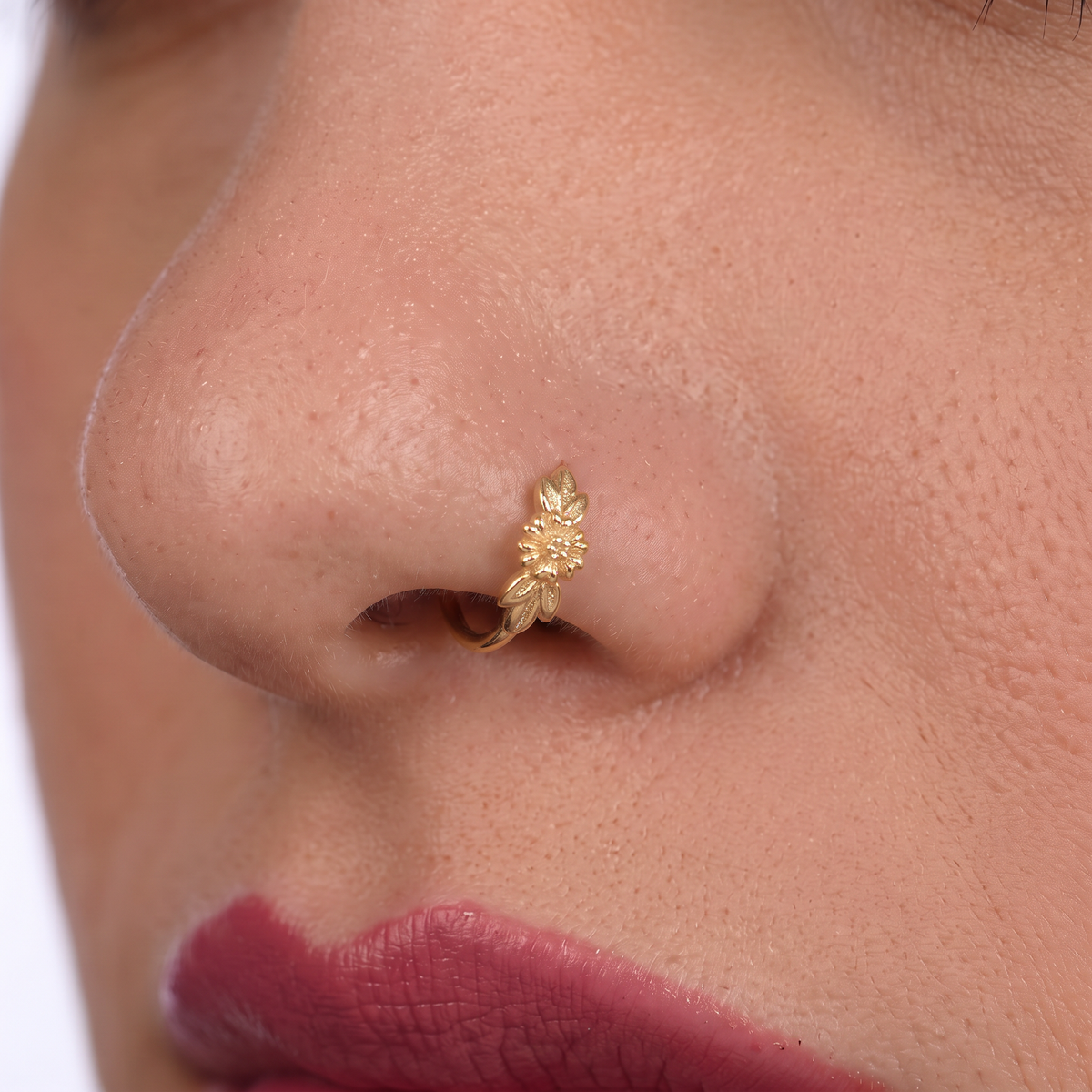 A close-up of a person's nose with a gold-colored nose ring featuring a leaf design.