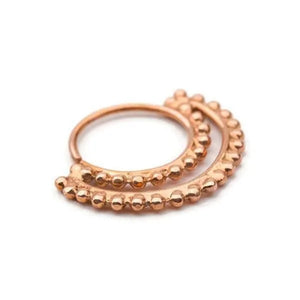 A copper-colored metal ring with a decorative, textured design featuring small, round beads or stones.
