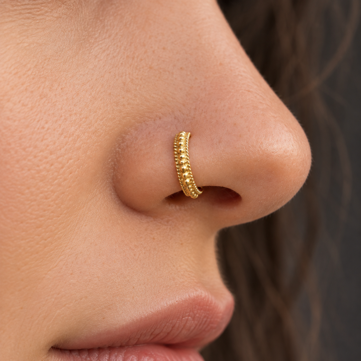 A close-up of a person's nose with a gold-colored nose ring.