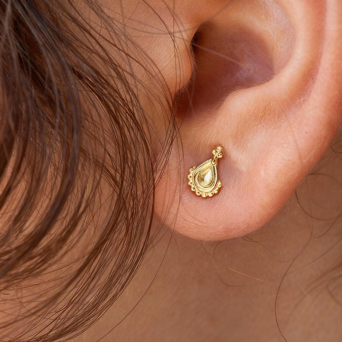 A close-up view of a person's ear adorned with a small, gold-colored earring featuring a decorative design.