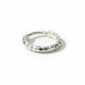 A silver ring with a unique, textured design rests on a dark, rocky surface.