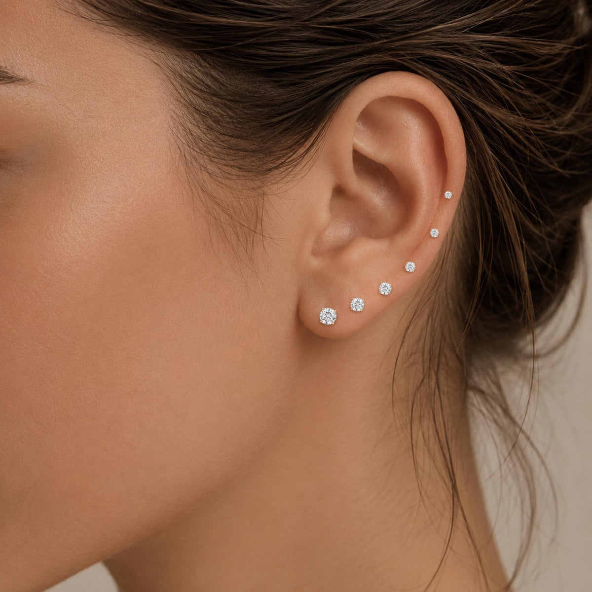 A close-up of a person's ear with multiple diamond earrings, including a row of earrings with a large diamond in the center.